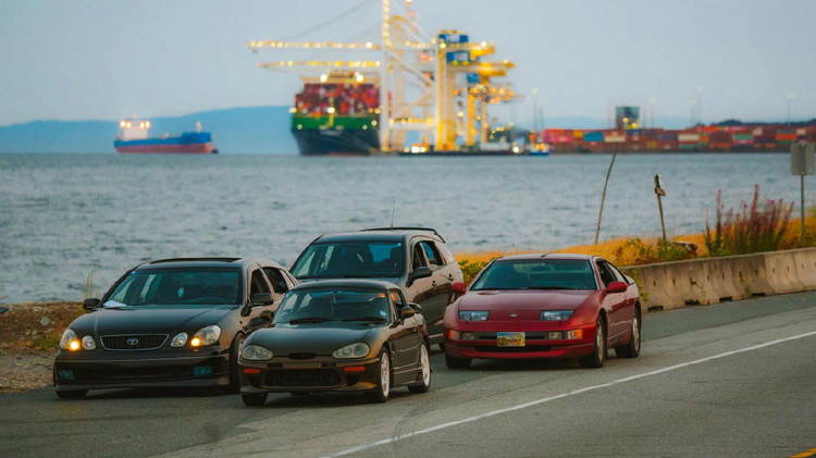 Vehicles ready for shipping at port with cargo vessels in the background.